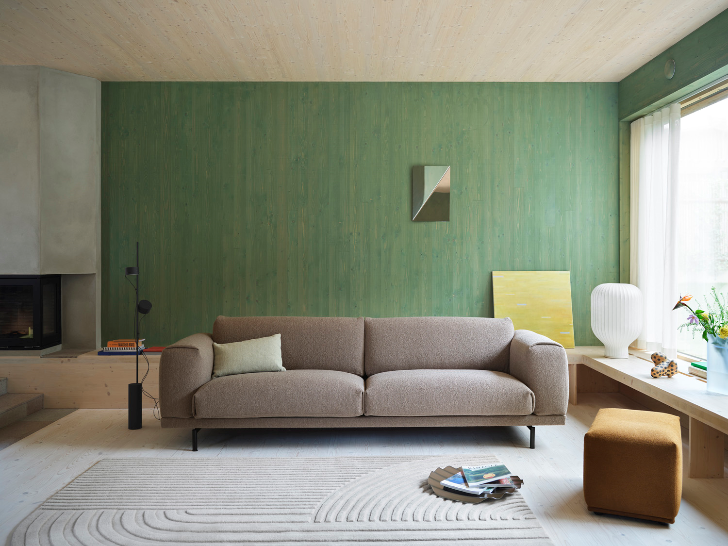 The Muuto Rest Sofa is elegantly styled with a burnt orange Relevo Rug and complemented by a Strand Table Lamp. A Gaze Mirror hanging on the wall adds a sophisticated, sculptural ambiance to the room.